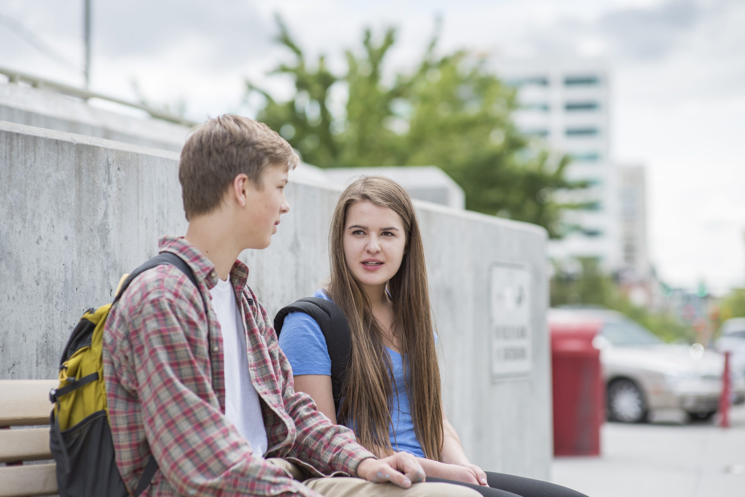 Two students sitting on a bench outside on campus talking.