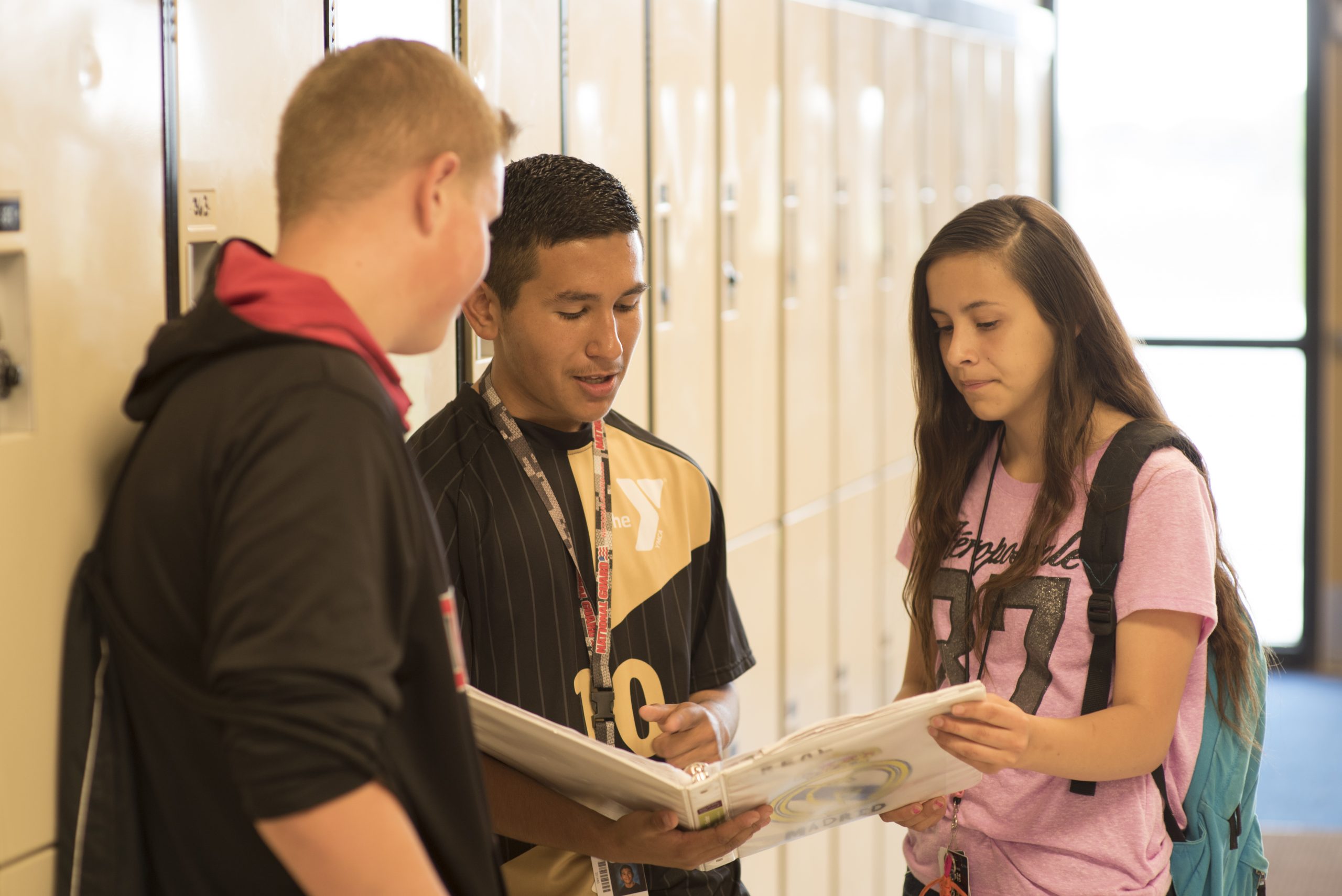 Three students reviewing contents of a binder in a school standing by lockers.