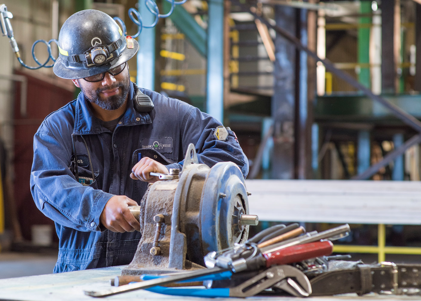 Man in hardhat and goggles using saw in an industrial setting.